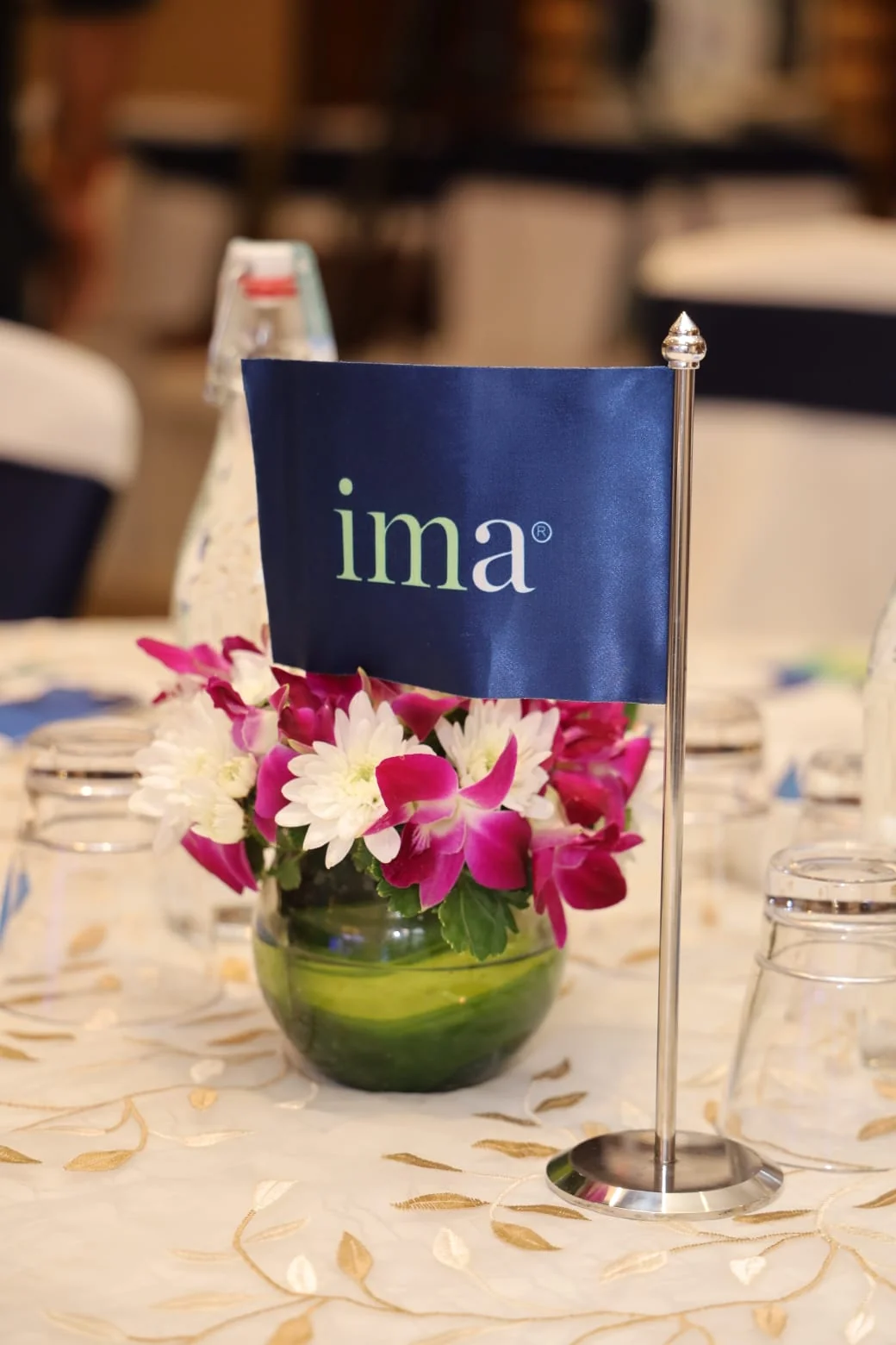 Conference table with IMA desk flag, flowers and branded materials at ima26 Mumbai